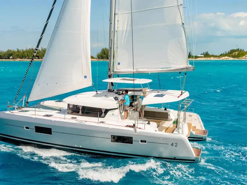Lagoon 42 catamaran under full sail along a turquoise coastline